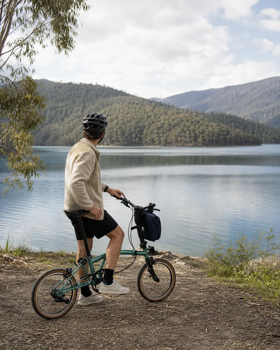 A traveller with a teal folder taking in the still water of an alpine lake.