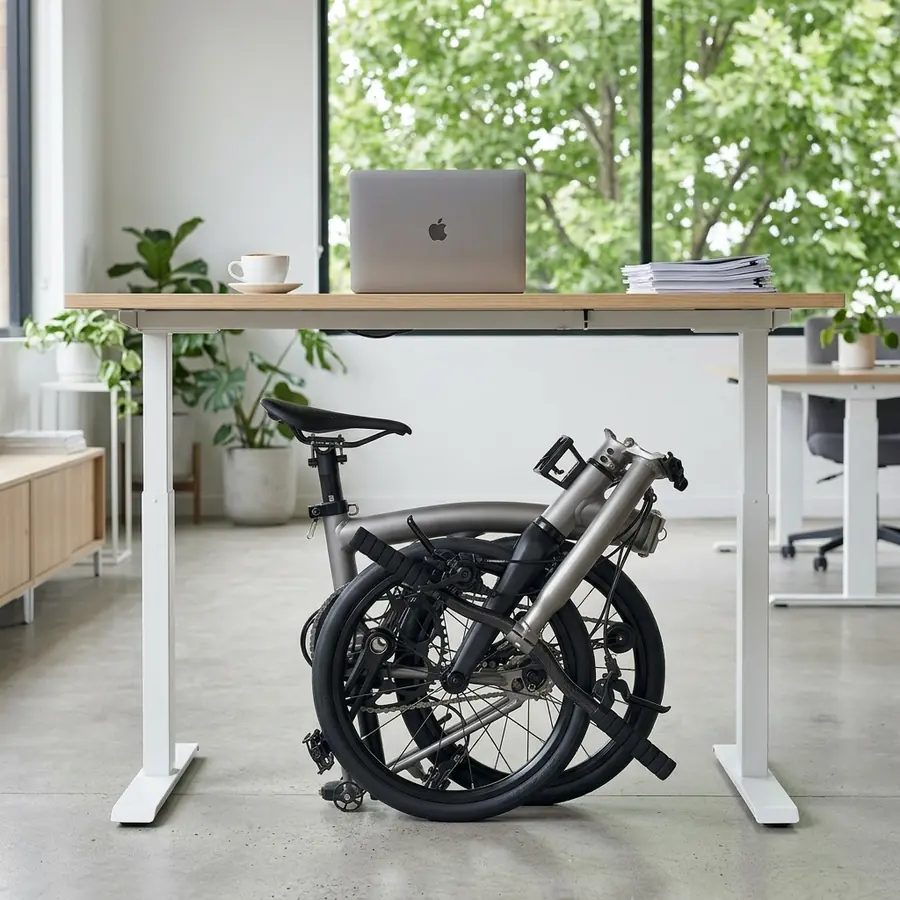 A silver Aerra folded under a standing desk in a sunlit office.